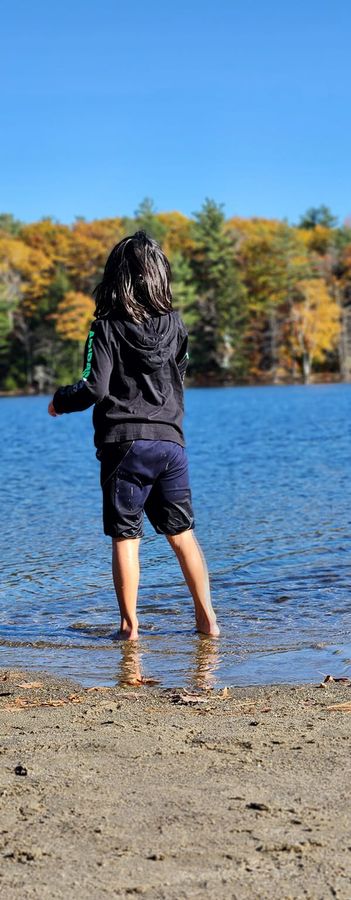 A child wading at the edge of a lake surrounded by autumn foliage