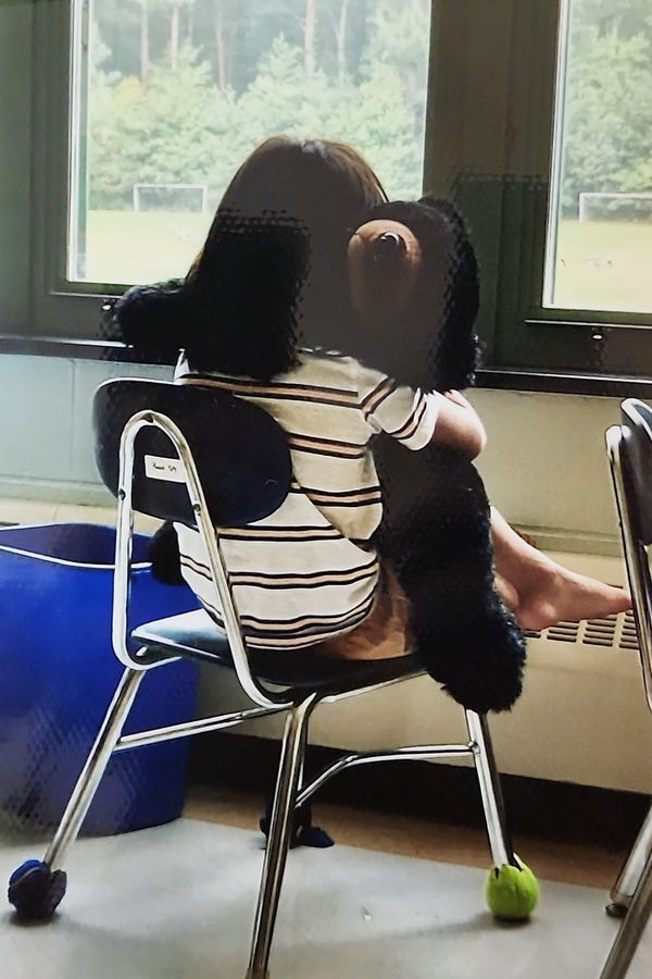 A child resting with a large soft toy in a classroom, chair legs fitted with tennis balls to reduce noise
