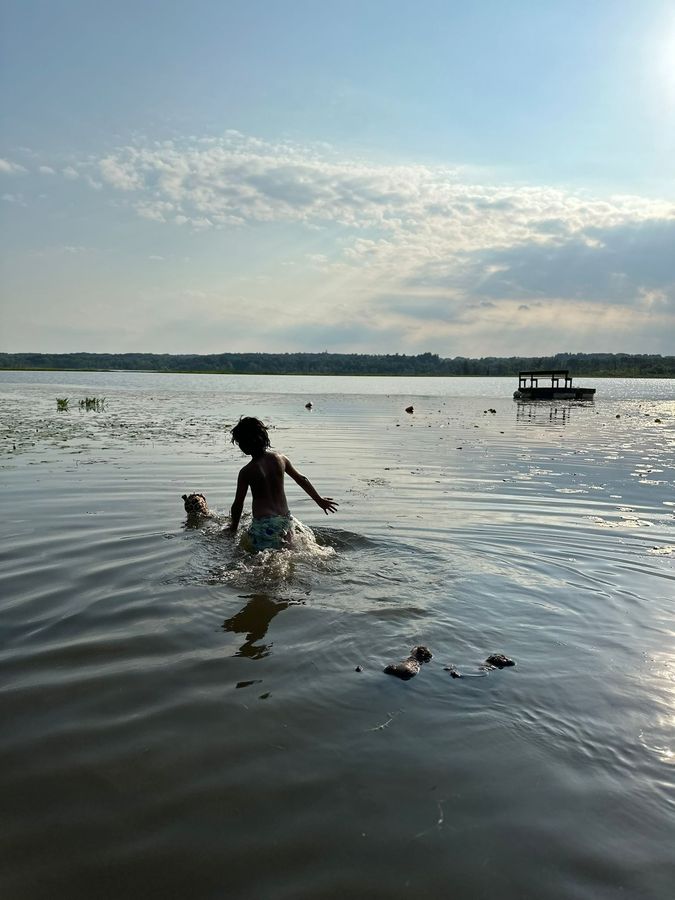 A child wading into a calm lake at golden hour, silhouetted against the water