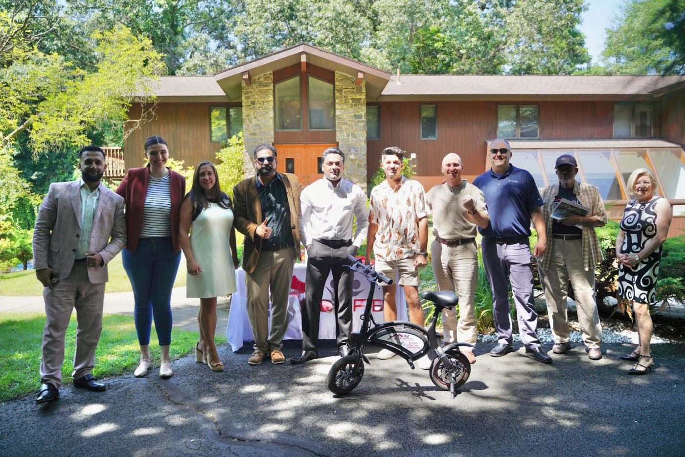 A group of adults standing outside a modern building on a sunny day, with an adaptive cycle in front of them