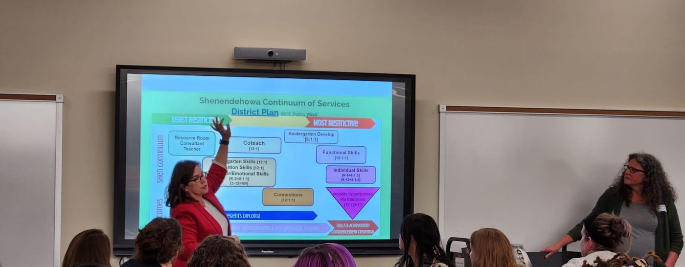 A presenter beside a screen showing the Shenendehowa Continuum of Services district plan diagram